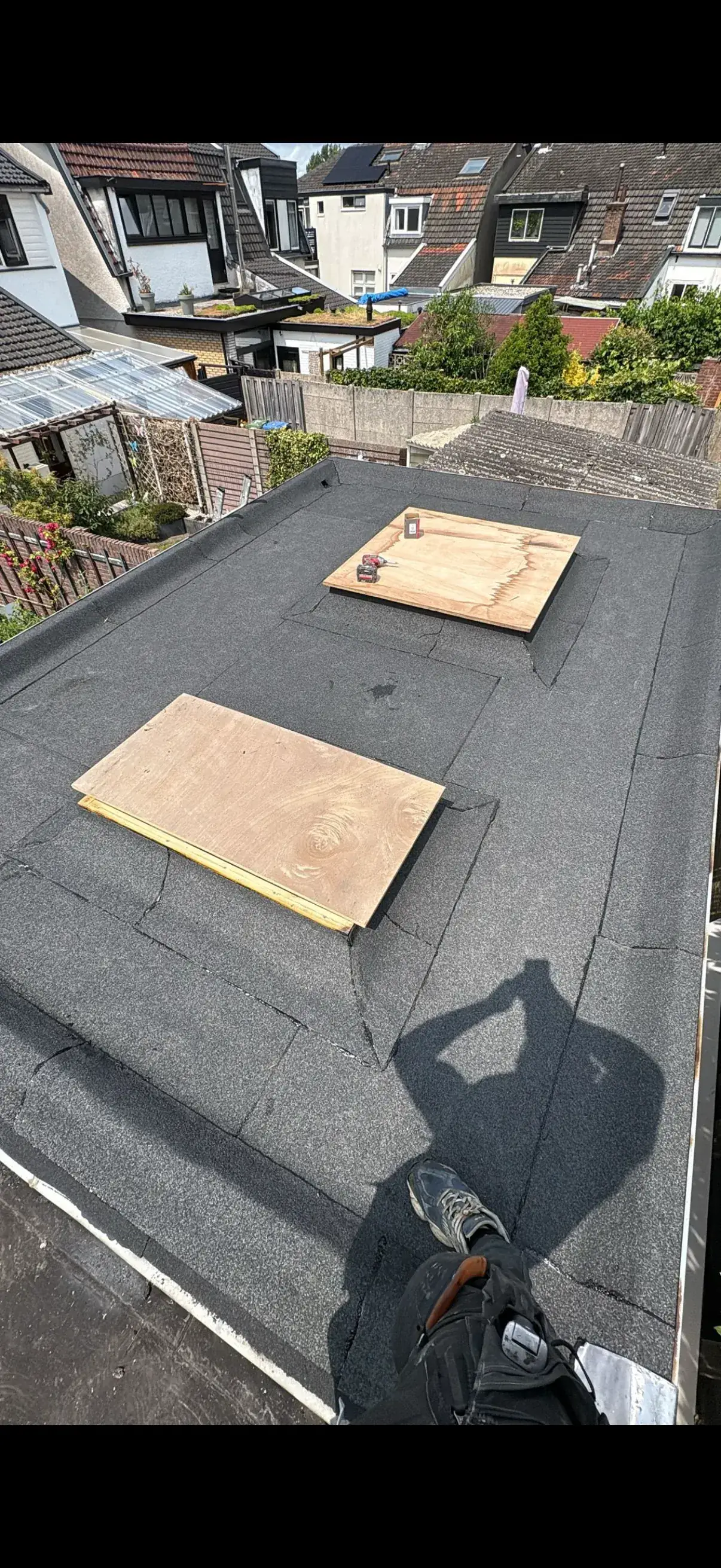 Nieuw aangebracht bitumen plat dak naast rood pannendak